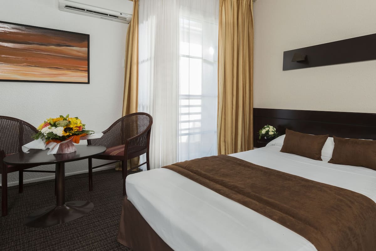 Une chambre d’hôtel avec un grand lit, un bureau avec une chaise, un vase de fleurs et un tableau au mur.