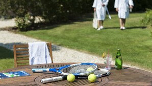 A round wooden table with a tennis racket, two tennis balls, a bottle, and a glass with a straw.