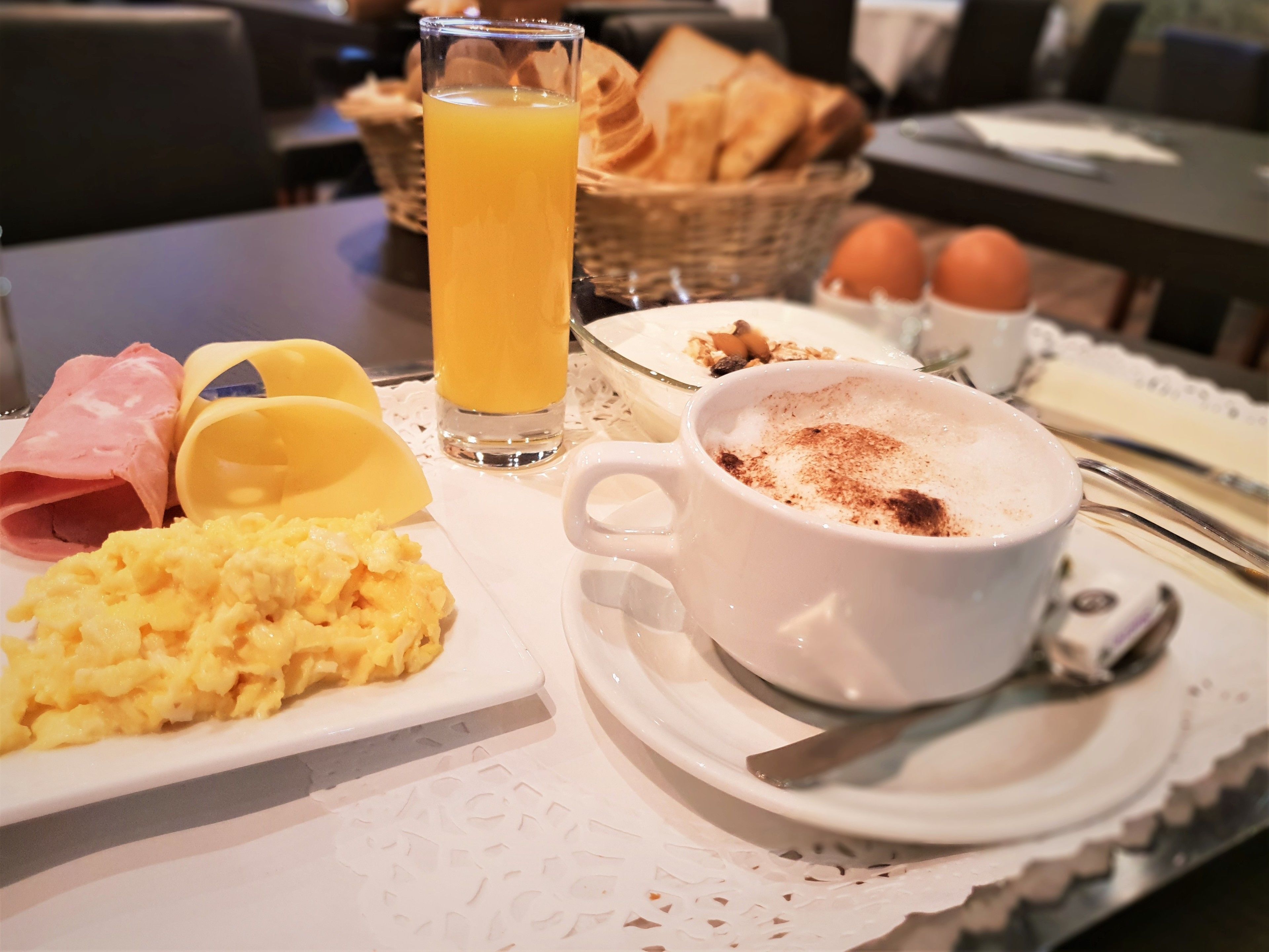 Un plateau de petit-déjeuner avec des œufs brouillés, du jambon, des toasts, du jus d’orange et une tasse de café saupoudrée de cannelle.