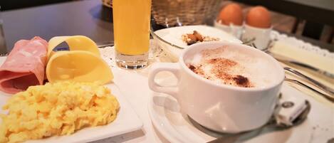 A breakfast tray with scrambled eggs, ham, toast, orange juice, and a cup of coffee with a sprinkle of cinnamon.