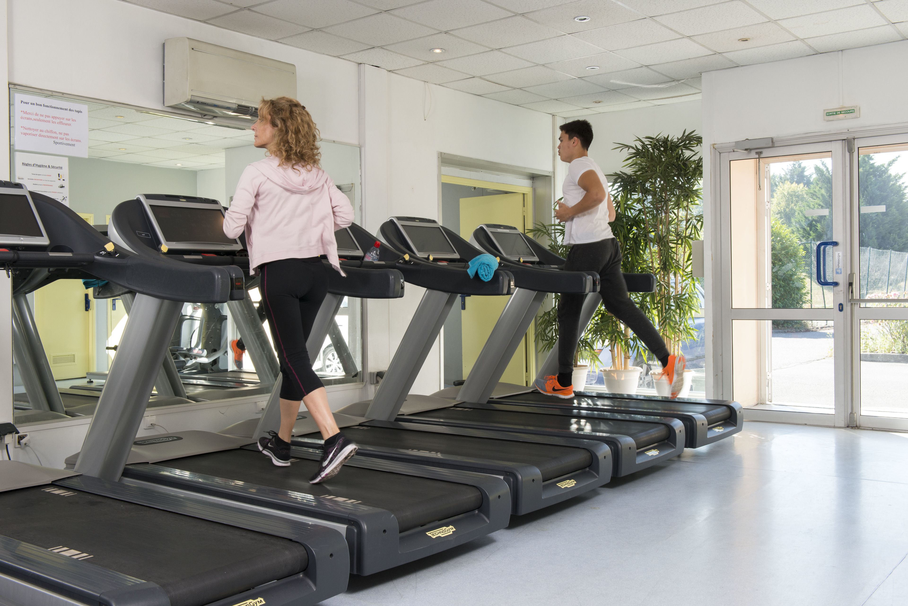 A gym with treadmills, a large mirror, and a potted plant.