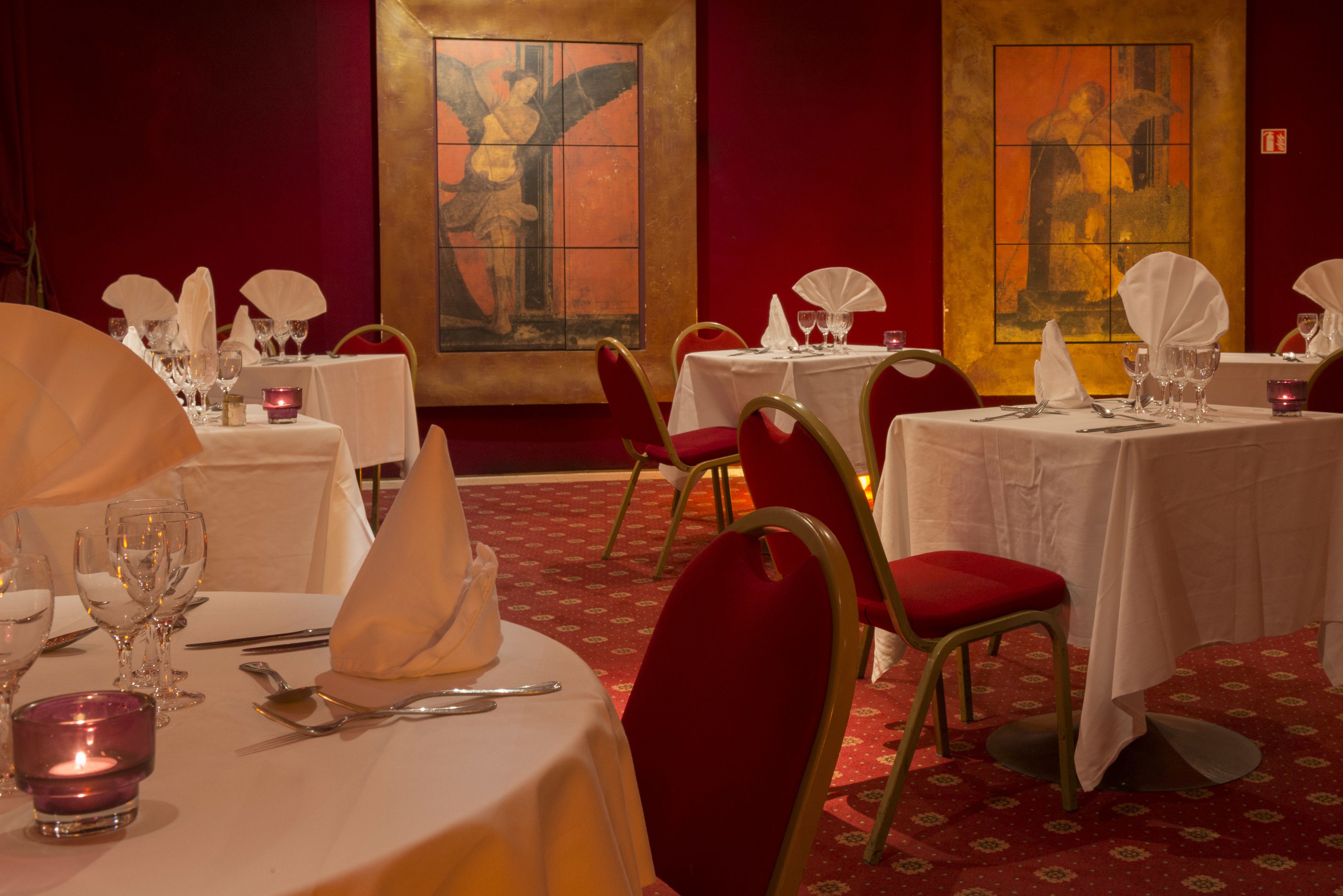 A restaurant with tables set for dining, red chairs, and artwork on the walls.
