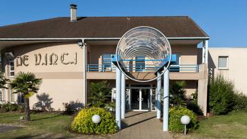 A building with a circular entrance structure, a sign reading "DE VINCJI", and a parking area with a blue line.