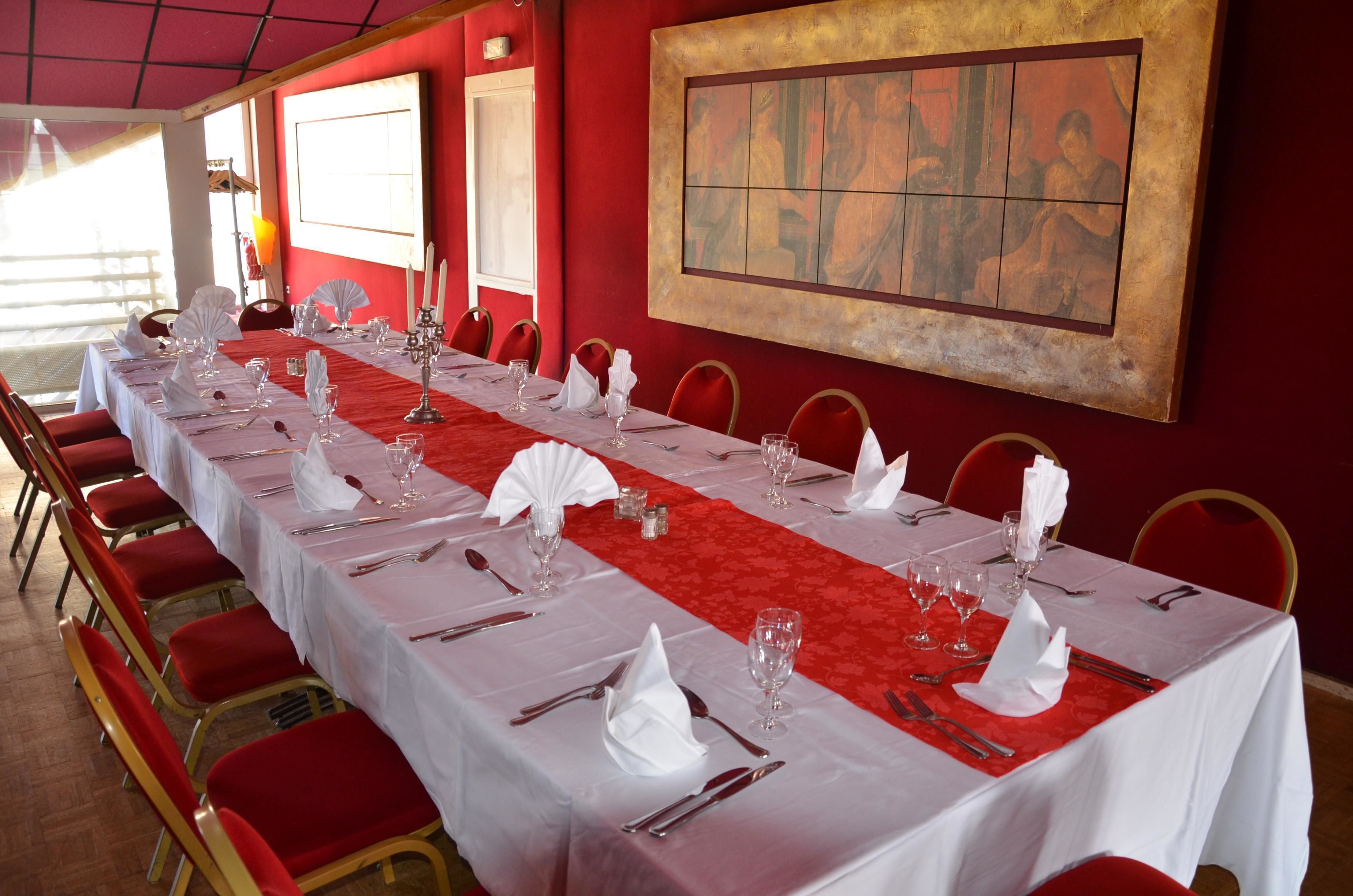 A long dining table set with white tablecloths, red chairs, and a red runner.
