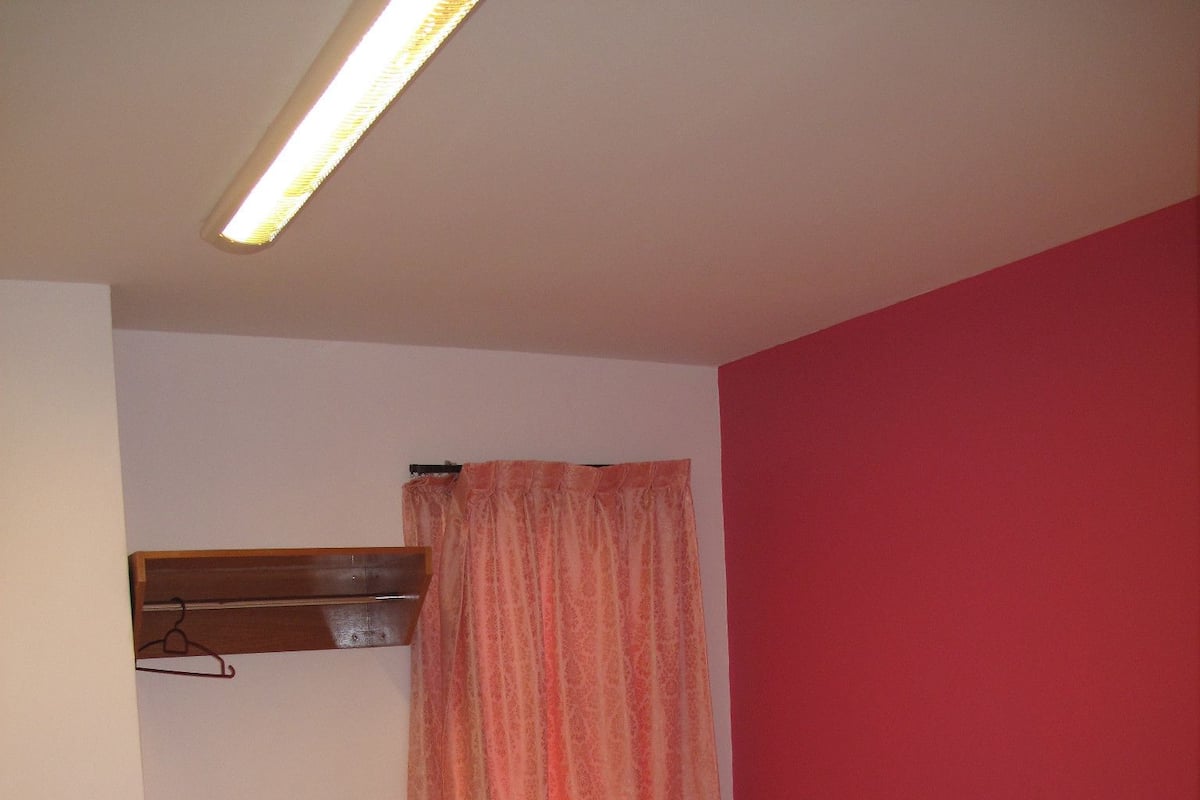 Ein kleiner, kompakter Raum mit zwei Einzelbetten, einem Holz-Kopfteil, einem kleinen Holzregal und einem Vorhang.