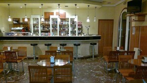 A bar area with multiple stools and tables, a counter with various bottles, and a television mounted on the wall.