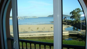 A coastal view from a balcony with a railing, a beach, and boats in the distance.