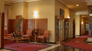 A lobby with a reception desk, seating area with chairs, a coffee table, and a red carpet.