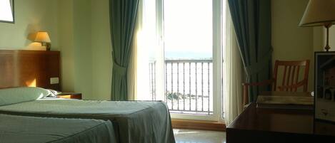 A hotel room with two beds, a desk, a chair, a lamp, and a balcony with a view.