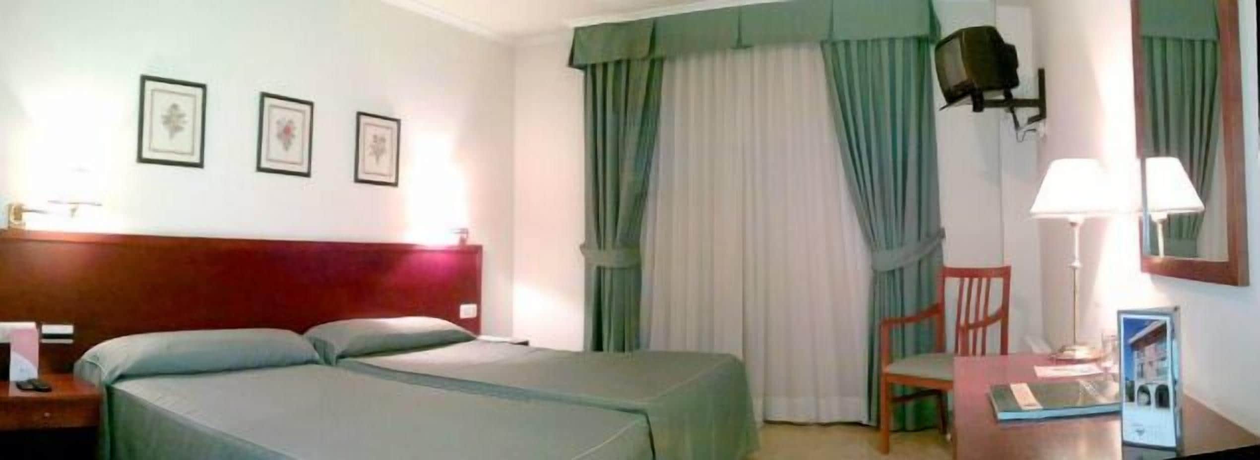 A hotel room with a bed, a chair, a desk, and a lamp.