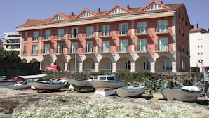 A multi-story building with balconies and arched windows, boats parked in front, and a clear sky.