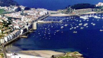 Vista aérea de un pueblo costero con un puerto deportivo lleno de barcos, una playa de arena y una mezcla de edificios residenciales y comerciales.