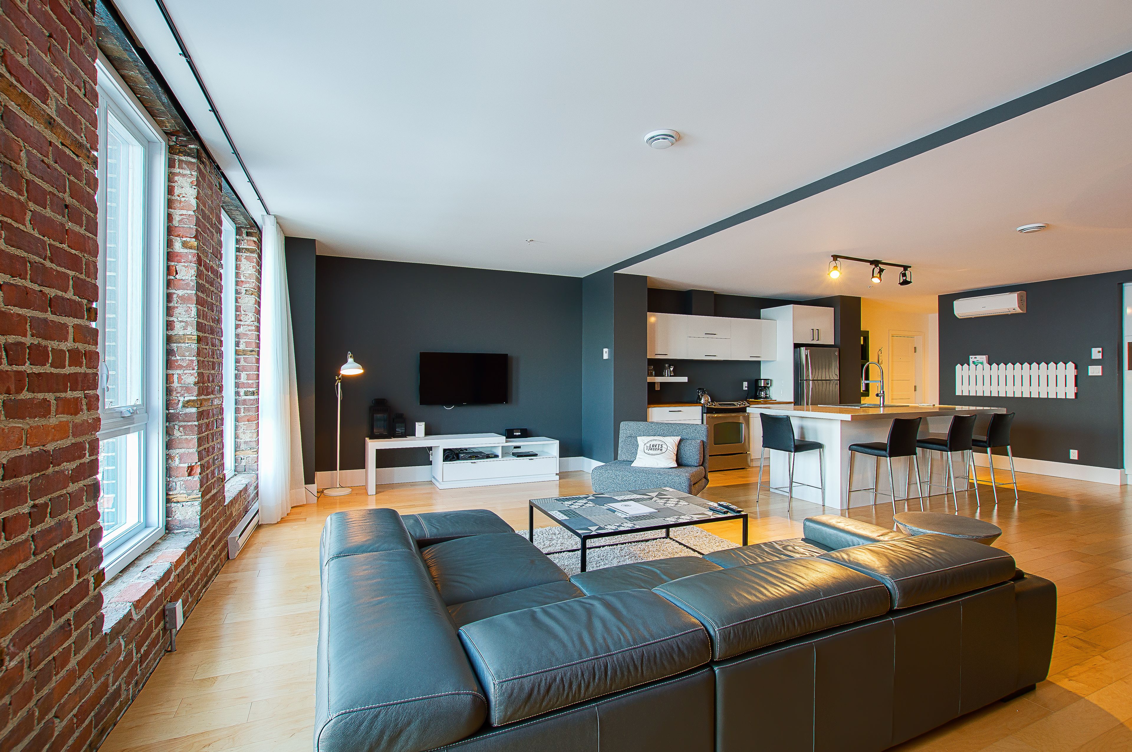 A modern living room with a large sectional sofa, a flat-screen TV, and a kitchen area with bar stools.