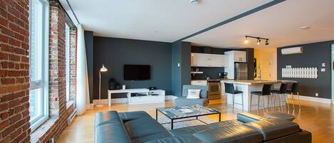 A modern living room with a large sectional sofa, a flat-screen TV, and a kitchen area with bar stools.