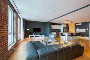 Una sala de estar moderna con un sofá modular grande, un televisor de pantalla plana y una zona de cocina con taburetes de bar.
