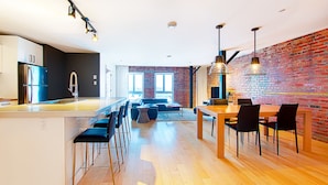 Een moderne keuken met een centraal eiland, barkrukken en een eethoek met een bakstenen muur en houten tafel.