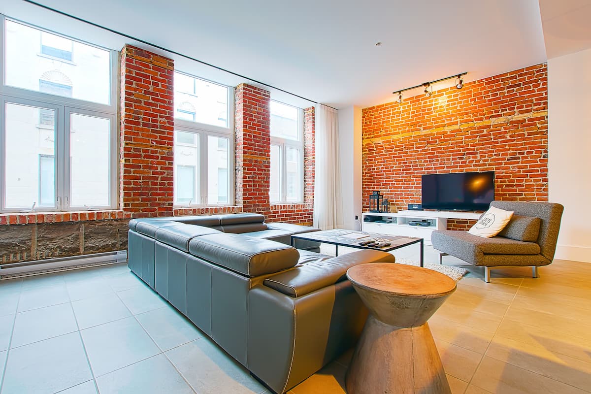 Una sala de estar moderna con pared de ladrillo, sofá de cuero y televisor de pantalla plana.