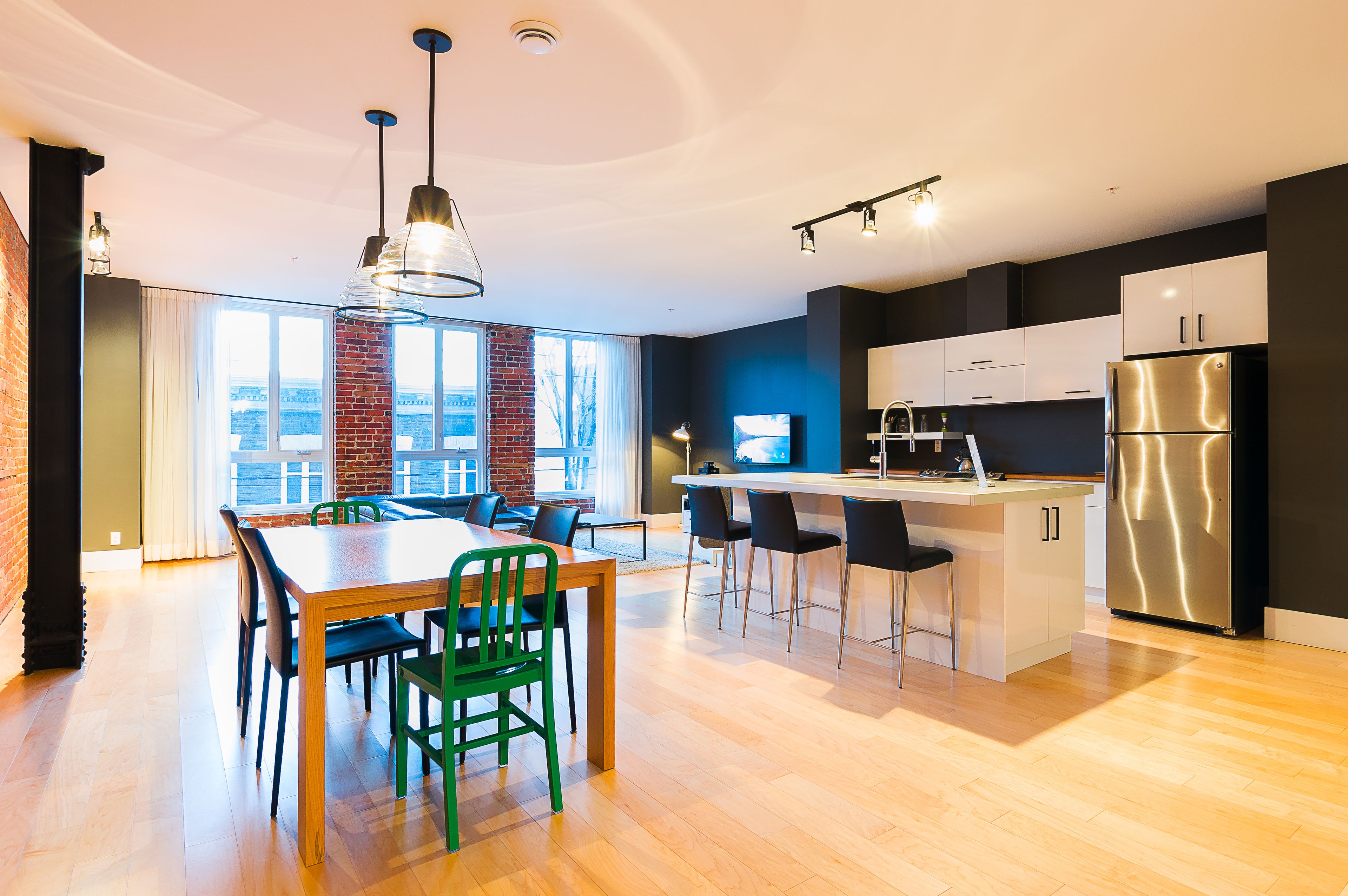 Una cocina moderna con comedor, ventanas amplias y un refrigerador de acero inoxidable.