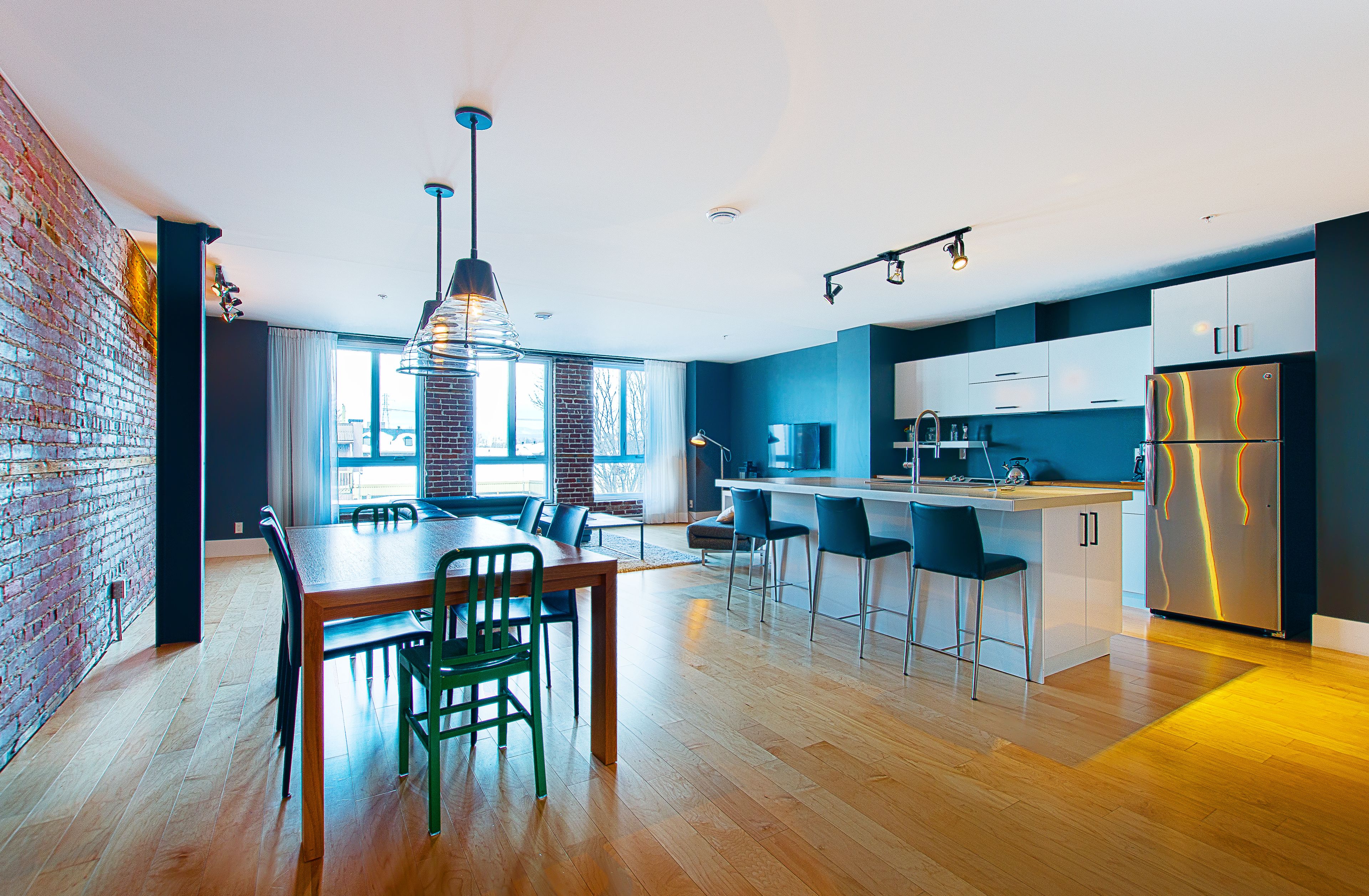 A modern kitchen with a brick wall, wooden flooring, and a stainless steel refrigerator.