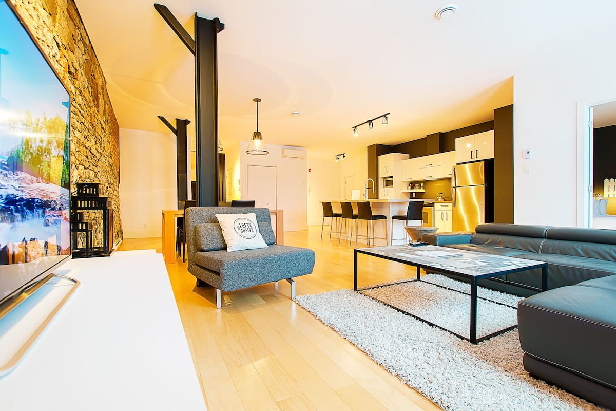Una sala moderna con un sofá, una mesa de centro y un televisor. Cuenta con una zona de cocina con armarios y un refrigerador.
