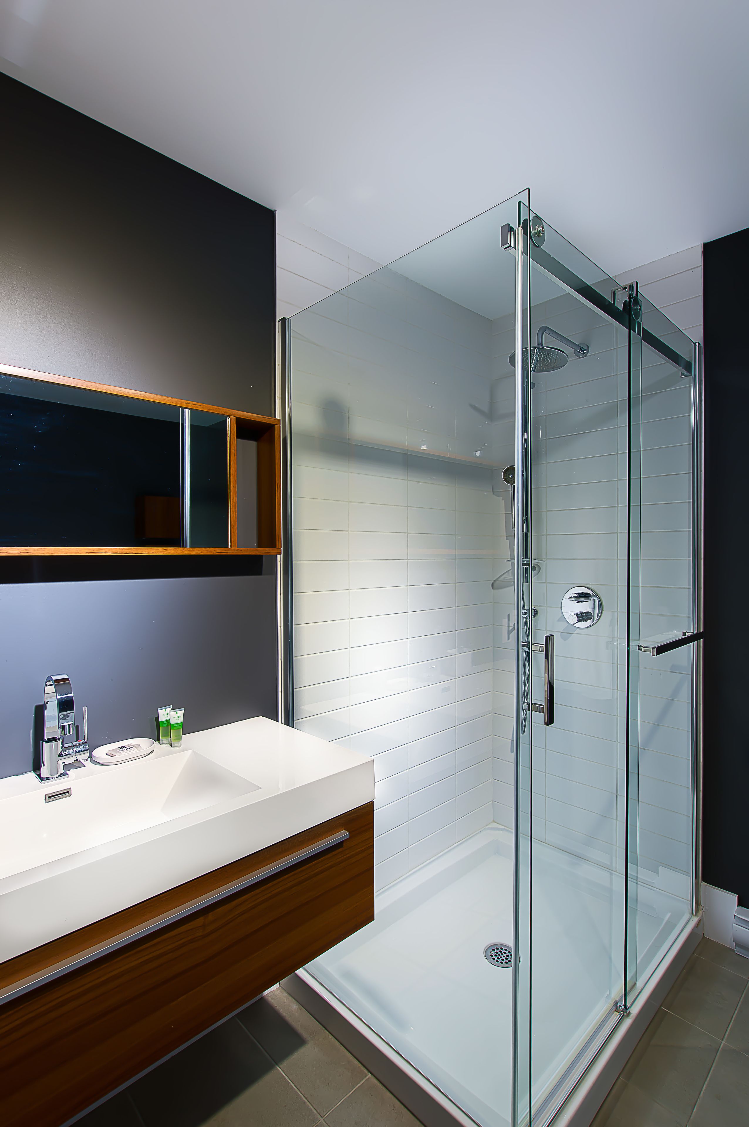 A modern bathroom with a glass-enclosed shower, a wooden vanity, and a mirror above the sink.