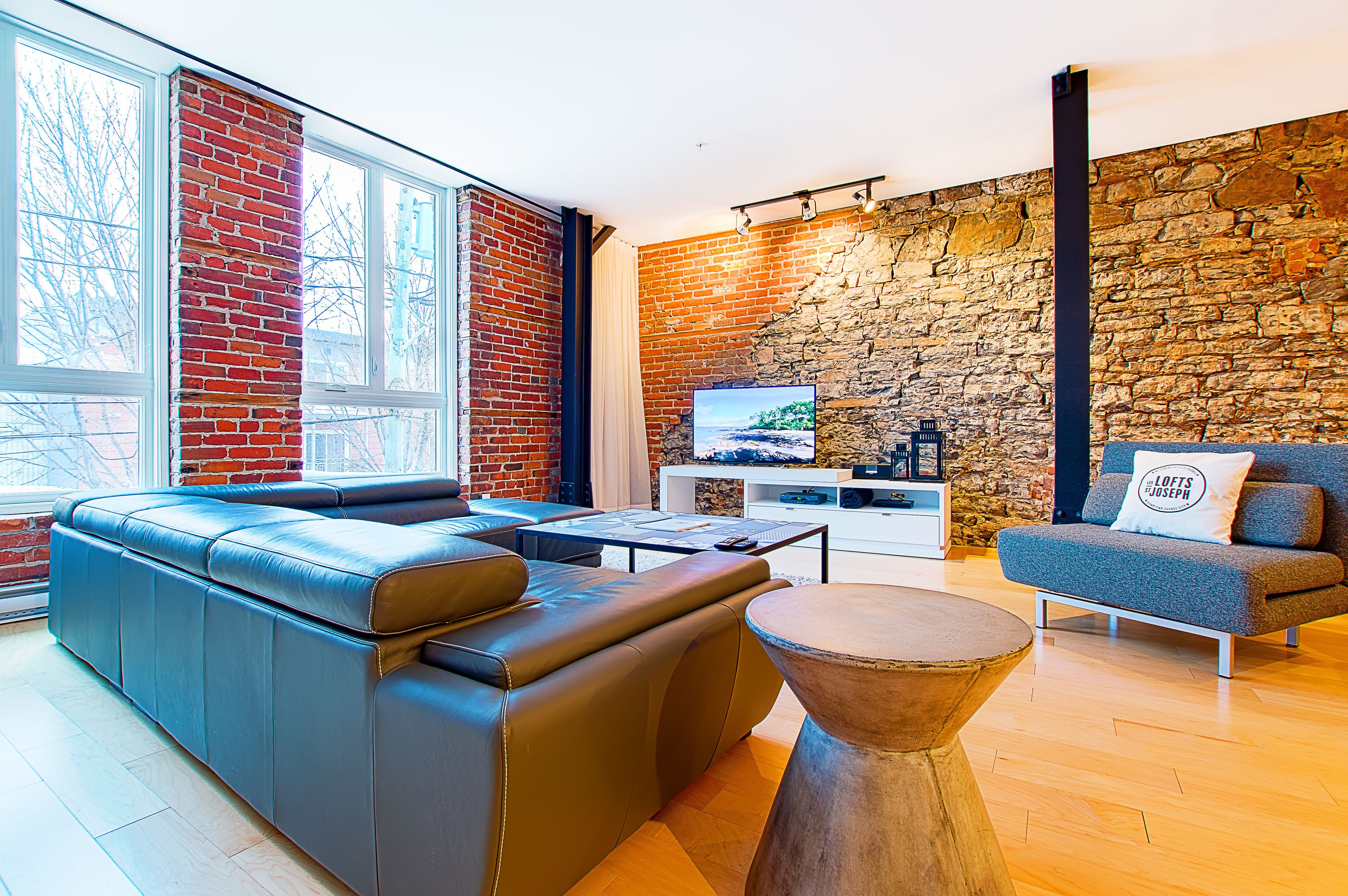 A modern living room with a leather sofa, a round wooden coffee table, and a stone wall.