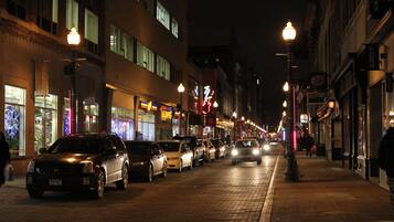Une scène de rue nocturne, avec des voitures garées et des devantures de magasins illuminées.