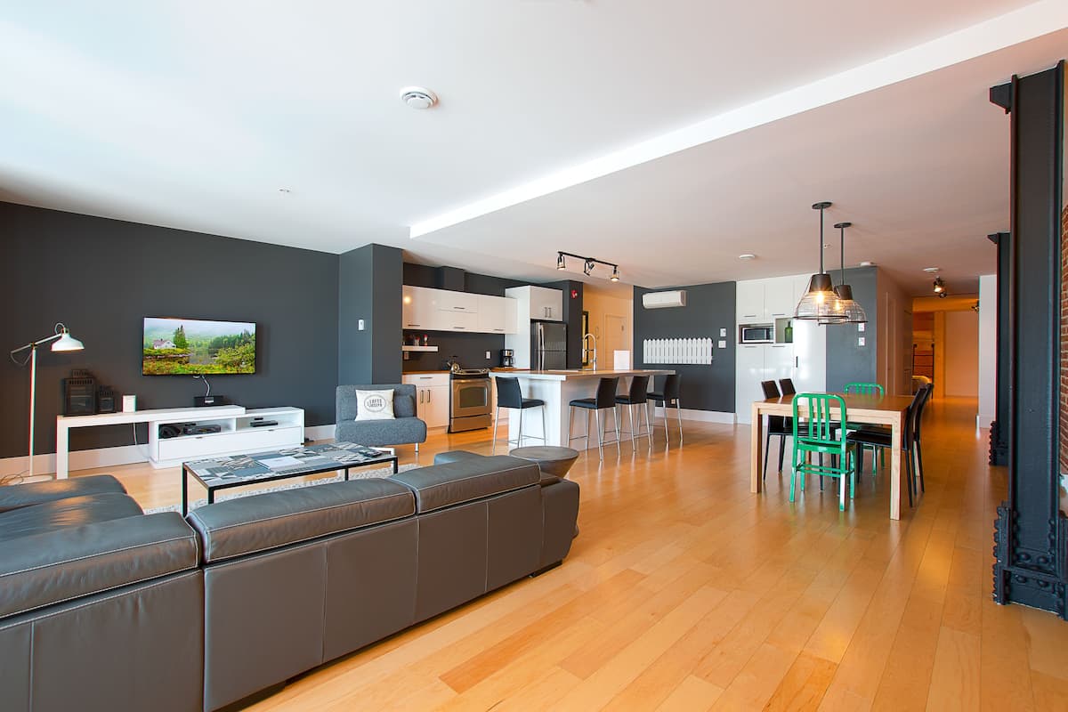 Una sala moderna con un sofá gris, un televisor y un comedor con una mesa y sillas.