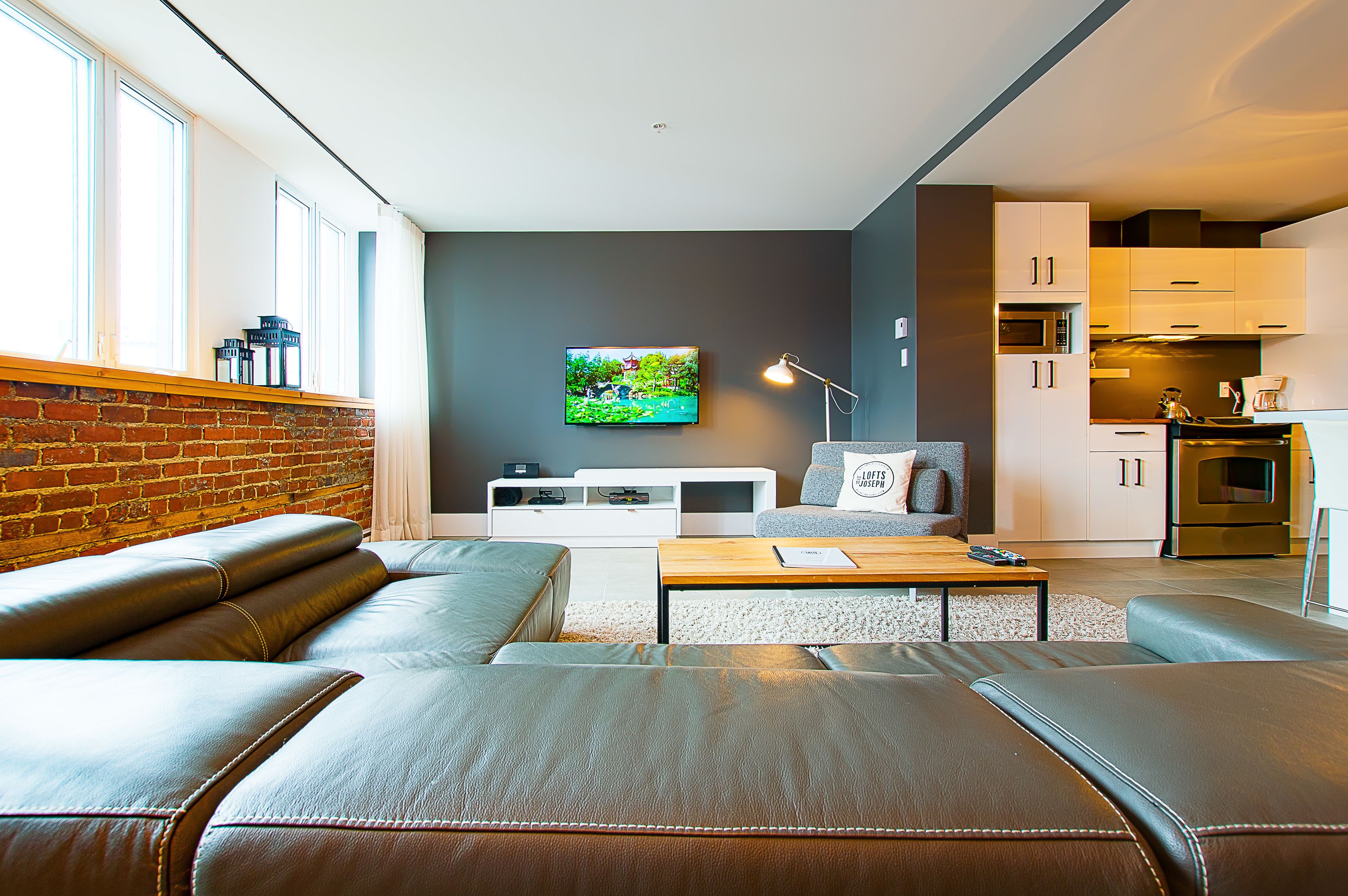 A modern living room with a leather sofa, a wooden coffee table, and a flat-screen TV mounted on the wall.
