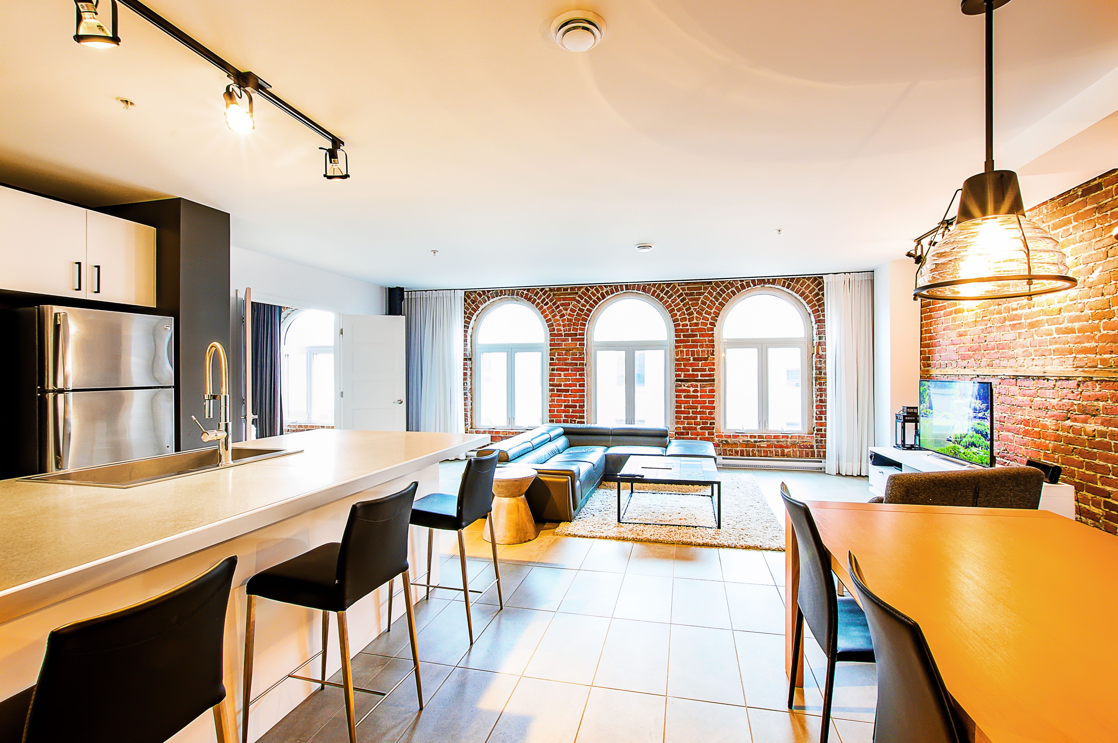 A modern kitchen with a large island, a dining area with a wooden table, and a living room with a sofa and a TV.