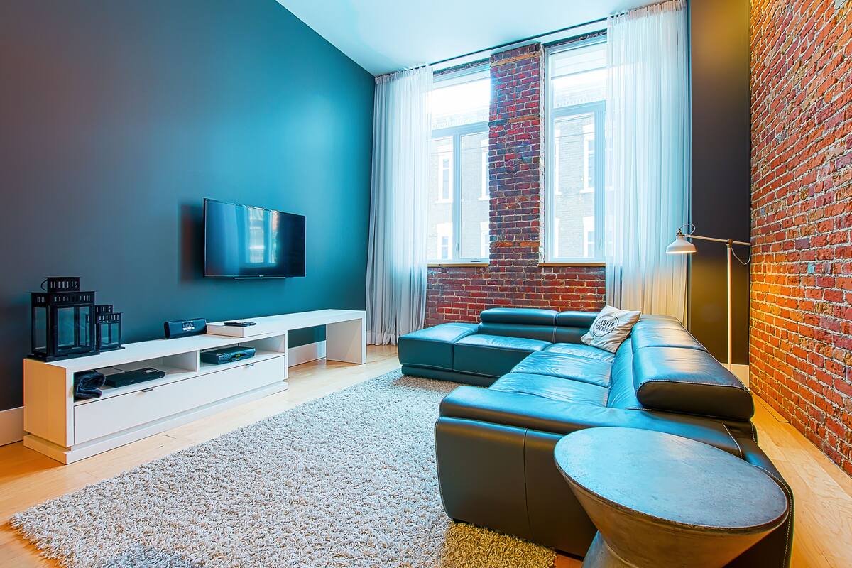 Una sala de estar moderna con un sofá seccional, un televisor de pantalla plana, un mueble blanco para entretenimiento y un amplio ventanal con vista a la ciudad.