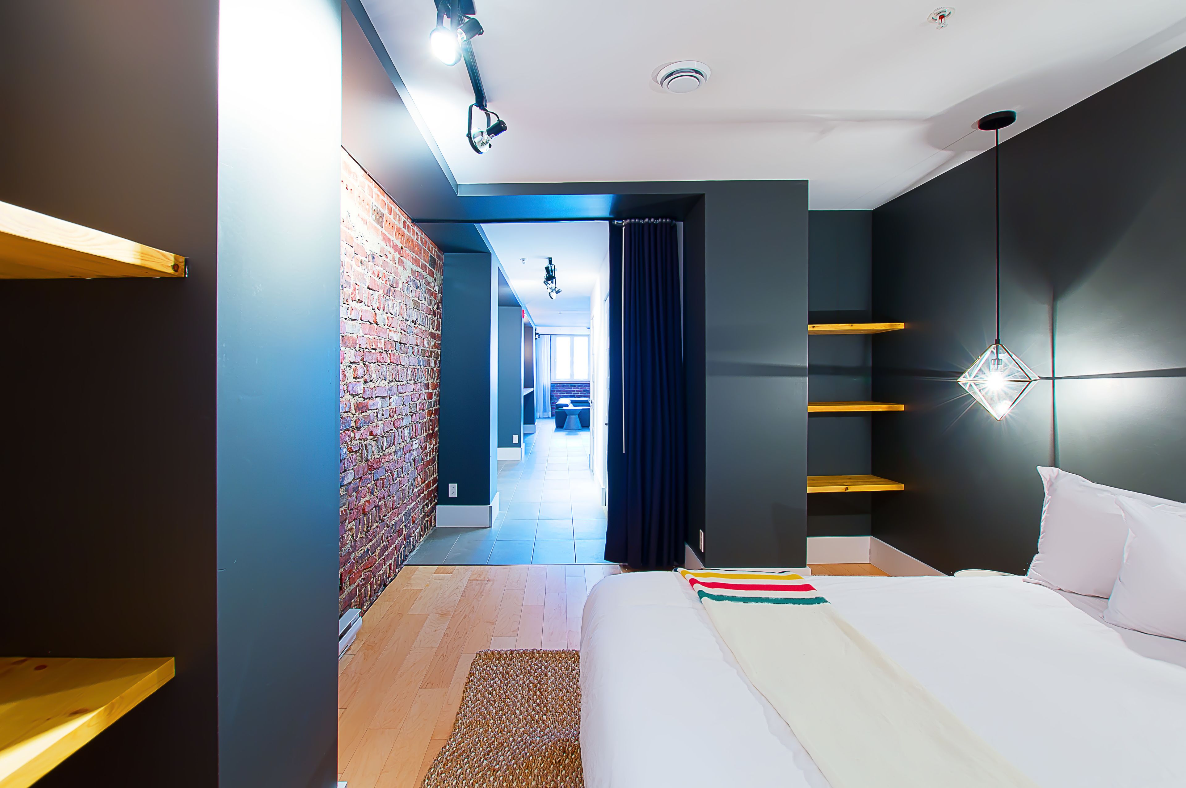 A modern bedroom with a brick wall, a bed with white bedding, and a ceiling light fixture.