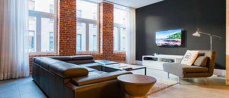Una sala de estar moderna con un sofá de cuero, una mesa de centro, una mesita auxiliar, un televisor montado en la pared y una pared de ladrillo decorativa.