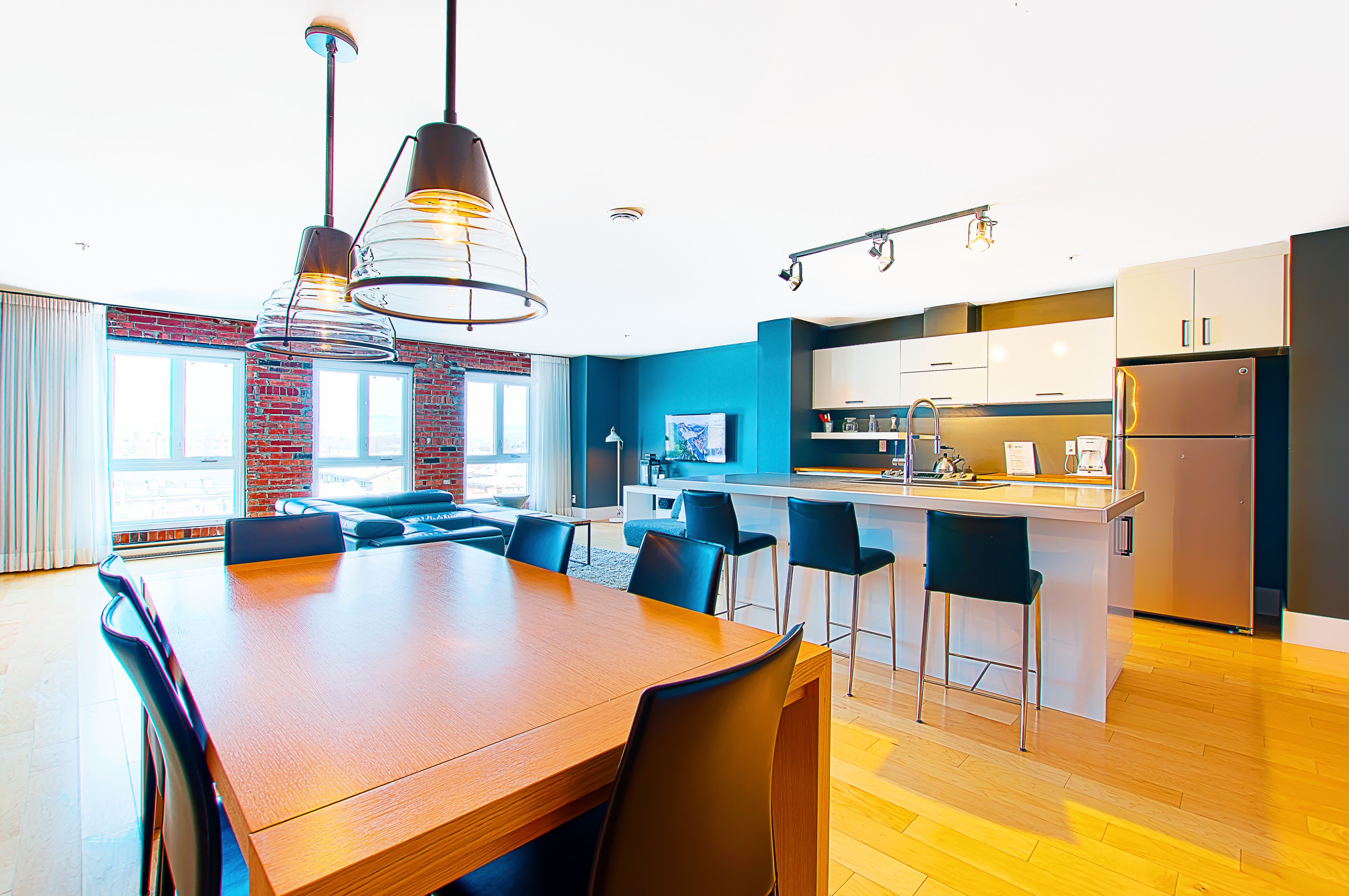 A modern kitchen with a central island, bar stools, and a dining table with chairs.