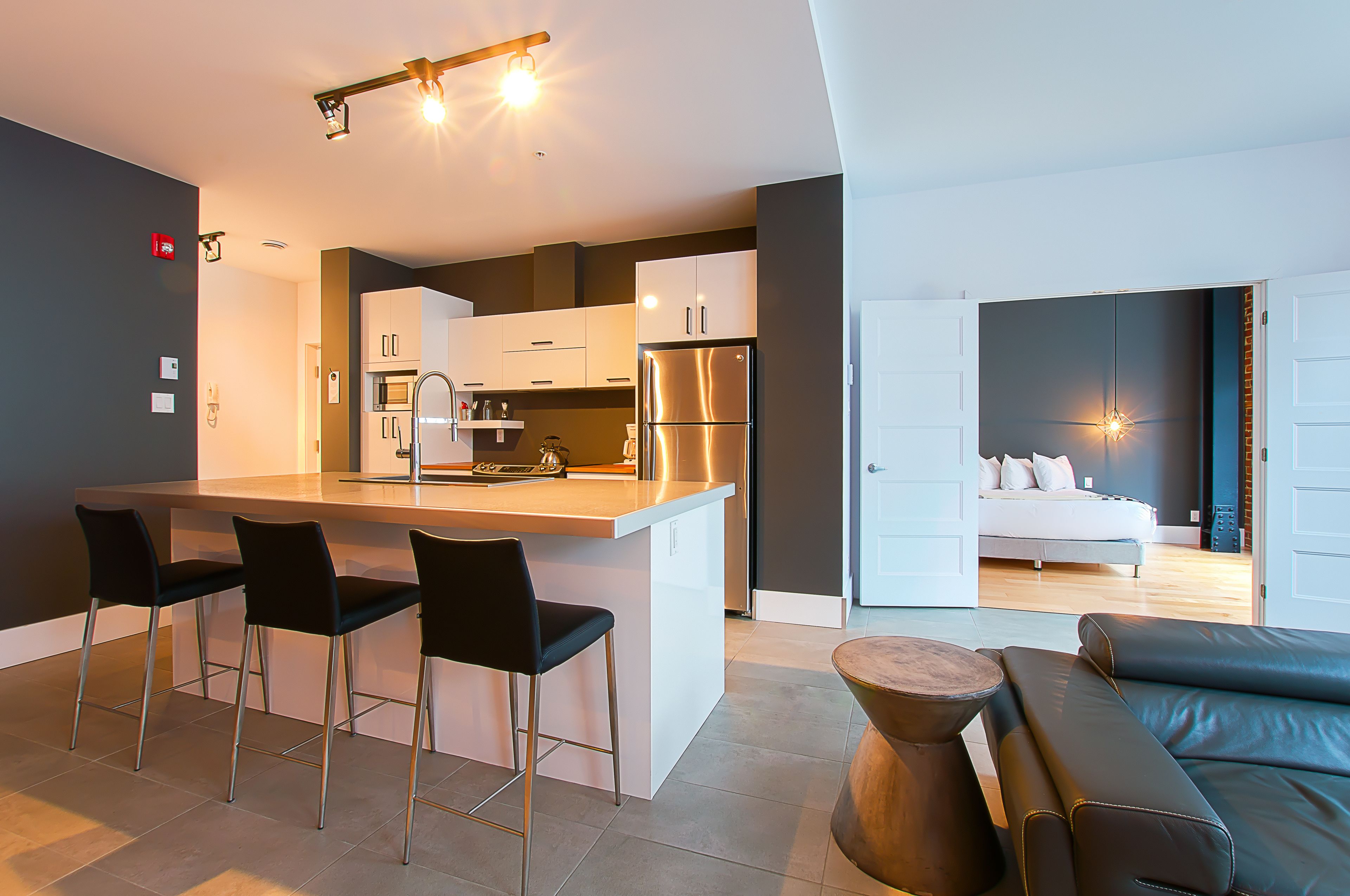 Una cocina moderna con una isla central, taburetes de bar y un comedor con sofá y mesa de centro.