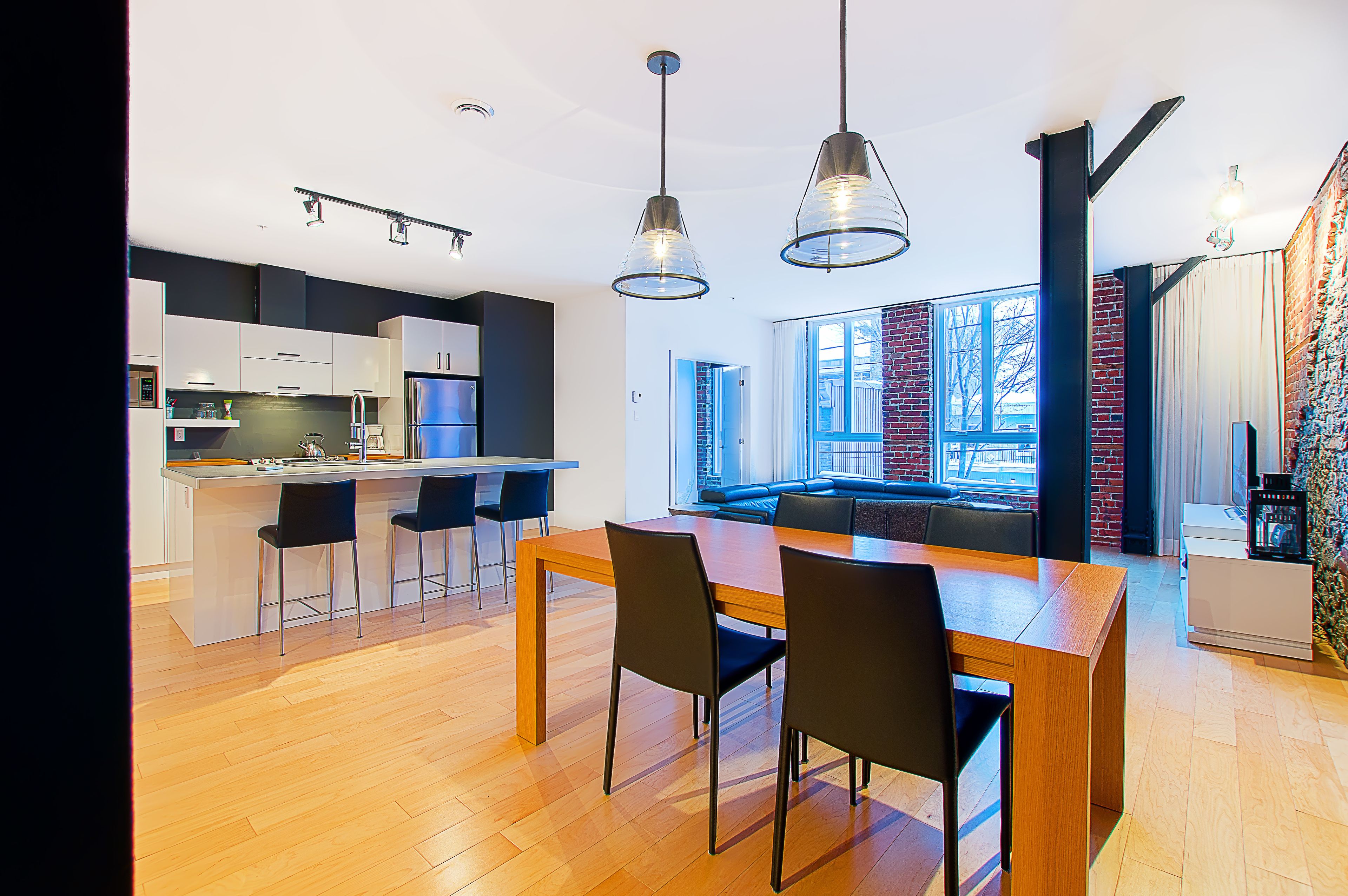 A modern kitchen with a central island, black chairs, and pendant lighting.