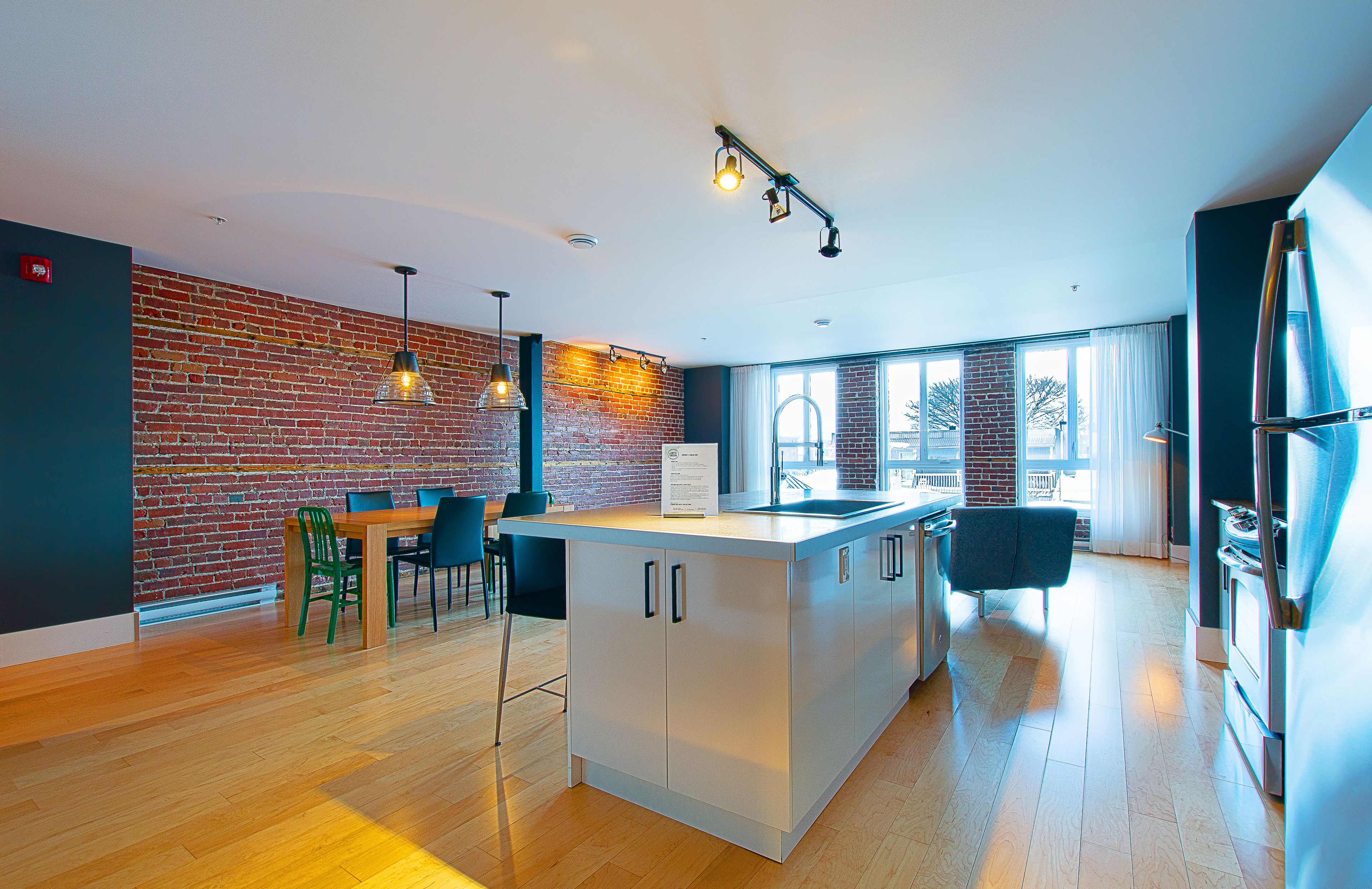 Una cocina moderna con una isla central, un muro decorativo de ladrillo y un comedor con sillas.