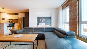 Una sala moderna con un sofá seccional, una mesa de centro de madera y una cocina al fondo.