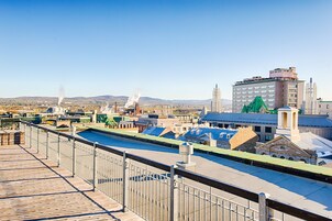 Vista desde la azotea de un hotel con piscina, una cerca metálica y un paisaje urbano al fondo.