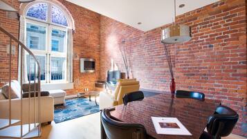 A modern living room with a brick wall, a large window, a sofa, a coffee table, and a dining table with chairs.