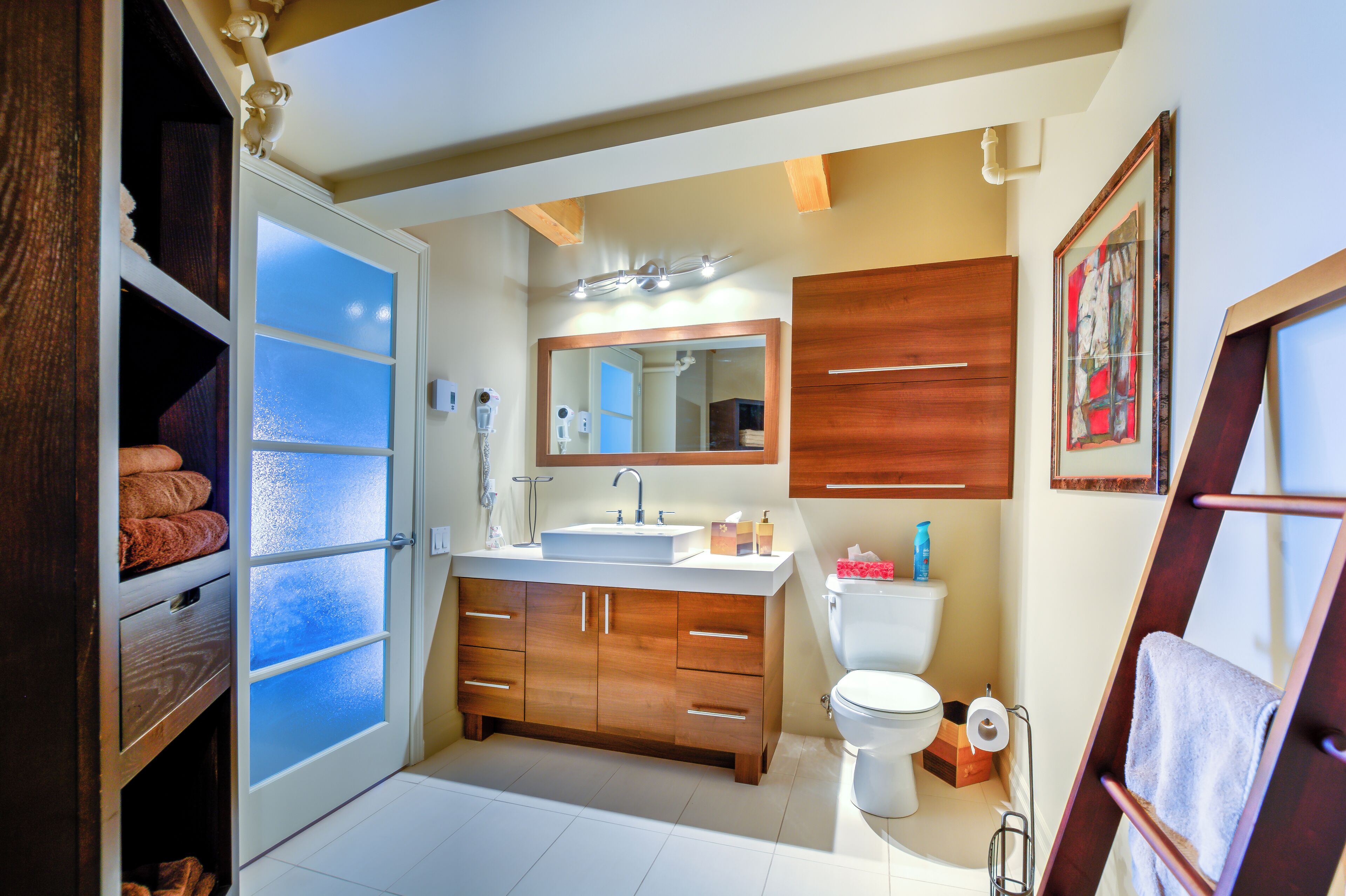 Une salle de bain avec un meuble-lavabo en bois, un grand miroir, des toilettes et un porte-serviettes.