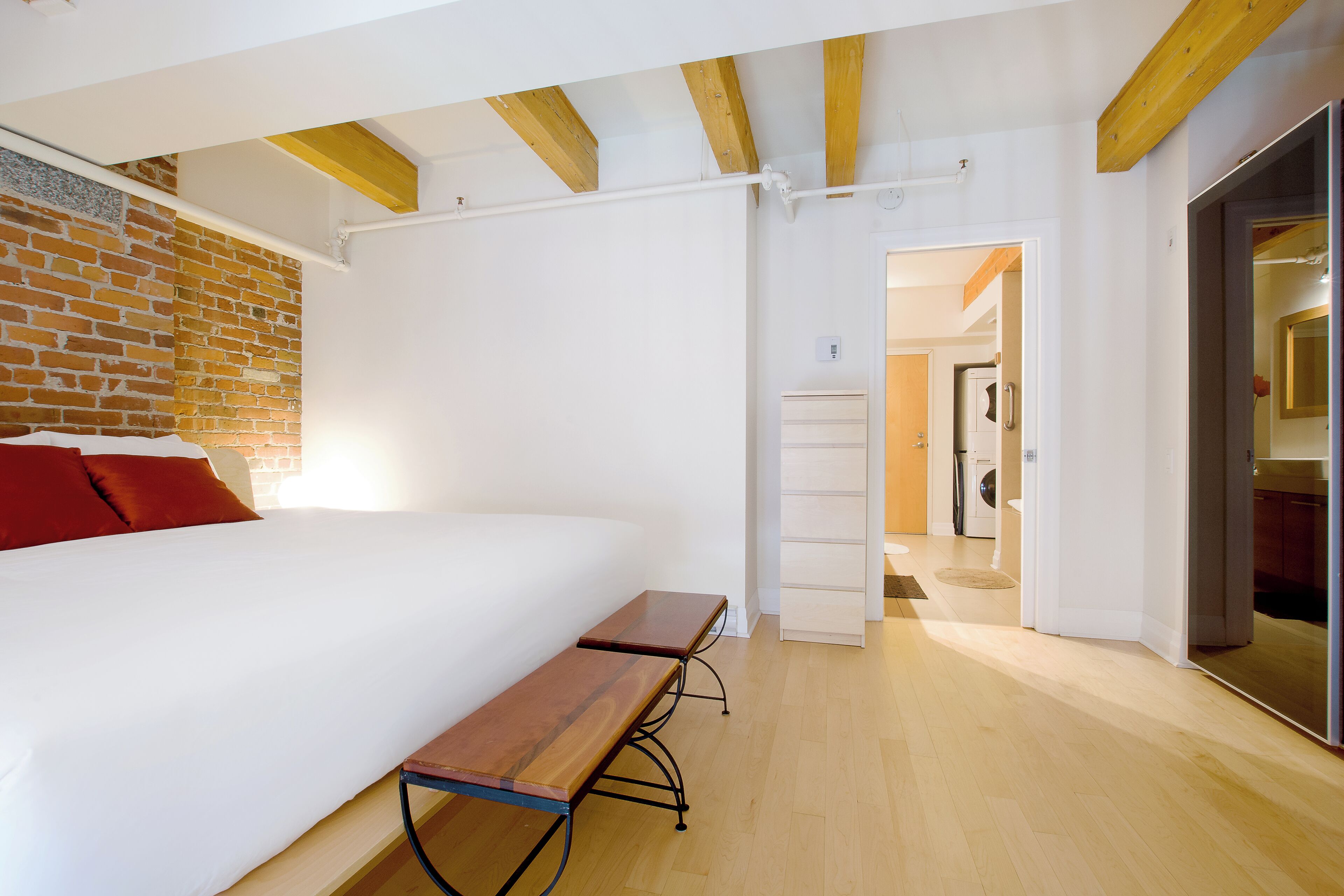 A bedroom with a large bed, a wooden bench, a brick wall, and a white ceiling.