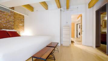 Ein Schlafzimmer mit einem großen Bett, einer hölzernen Bank, einer Ziegelwand und einer weißen Decke.