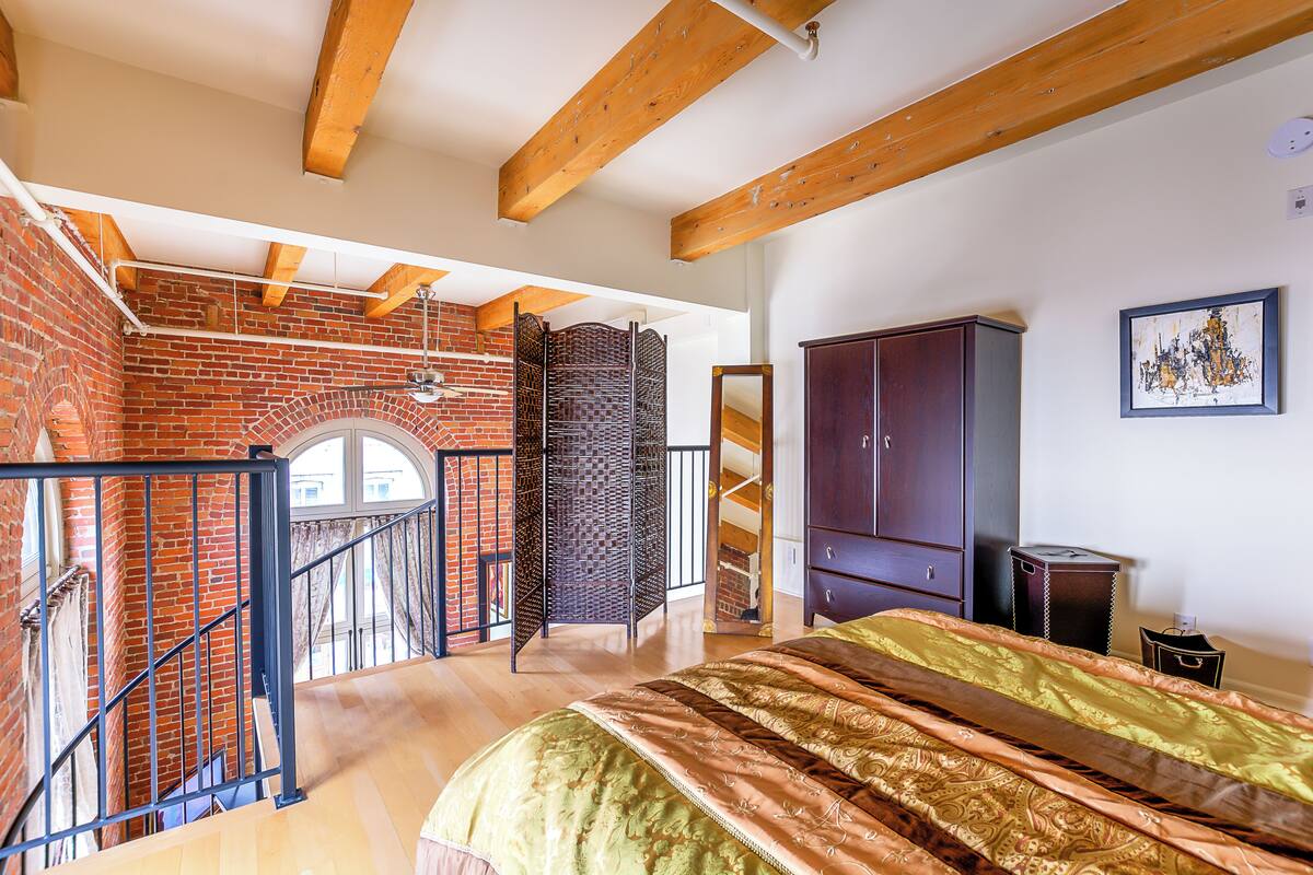 A bedroom with a bed, wooden beams, a brick wall, and a balcony.