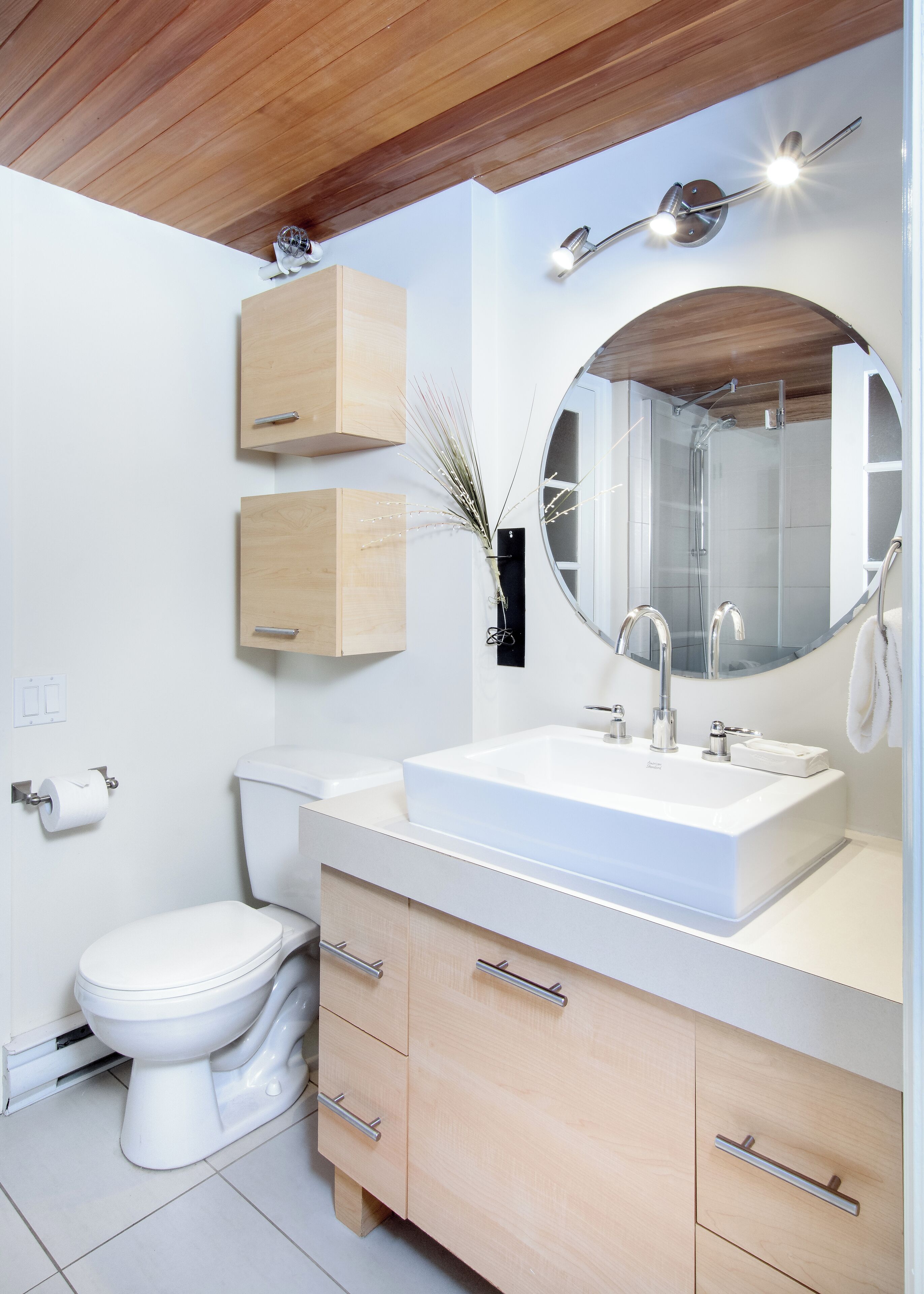 Une salle de bain moderne avec un lavabo blanc, un grand miroir et des meubles en bois.