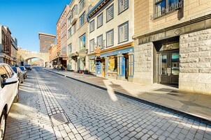 Una calle adoquinada bordeada por edificios históricos, un coche blanco estacionado a la izquierda y un cielo azul despejado.