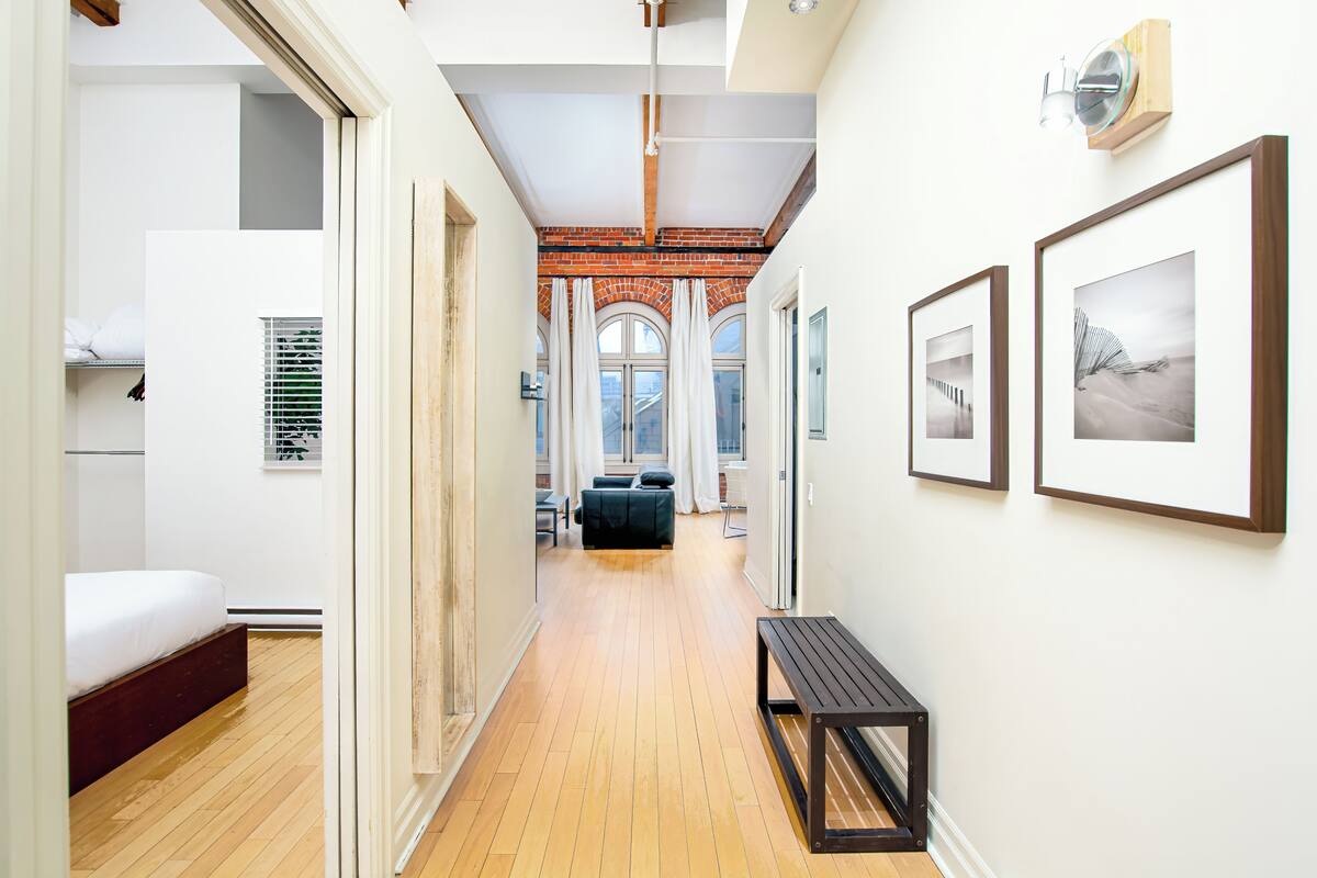 A hallway with a wooden floor, a bench, and framed artwork on the walls.