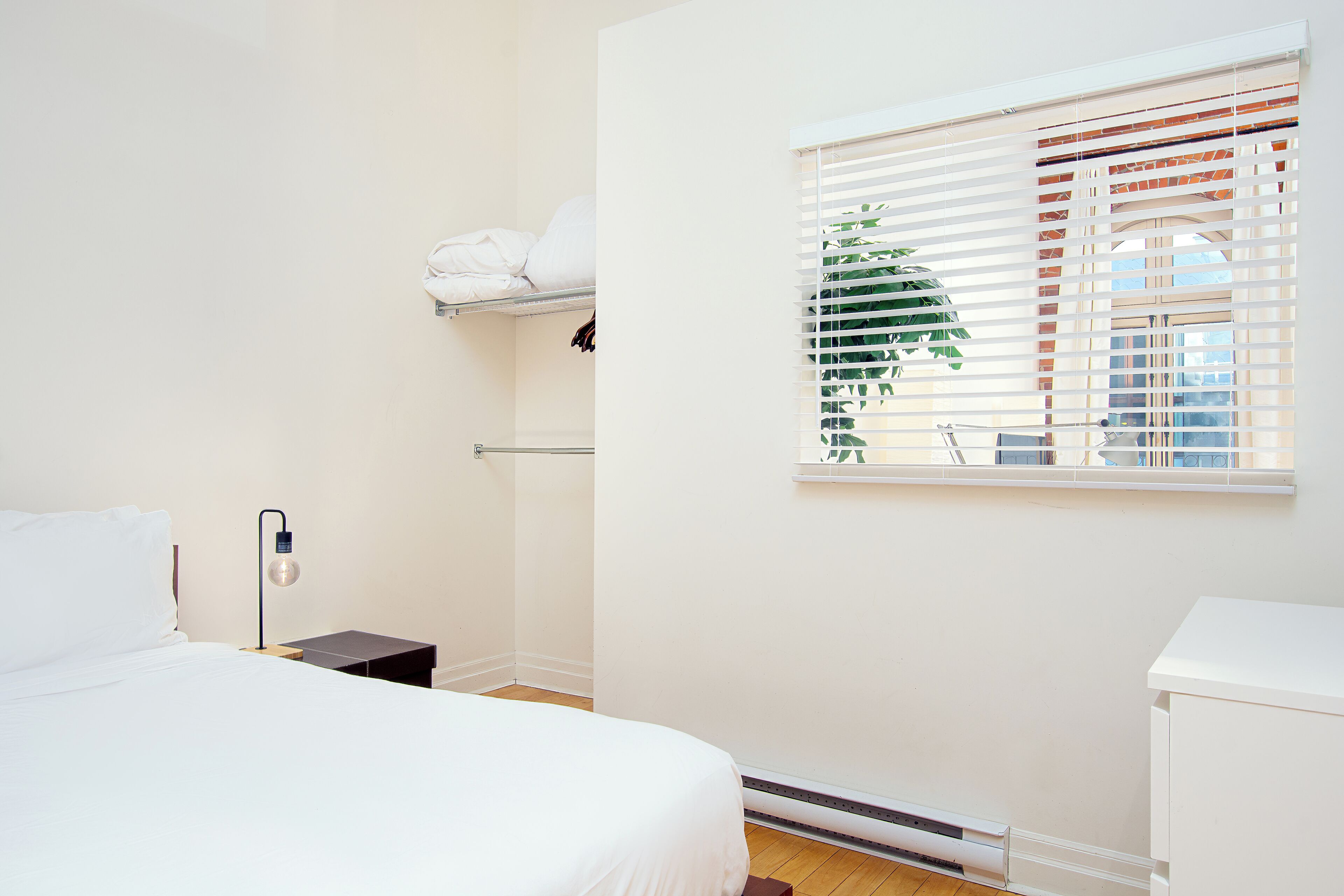Un dormitorio con cama, mesita de noche, lámpara y ventana con persianas.