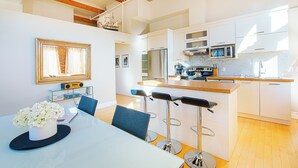 A modern kitchen with white cabinets, stainless steel appliances, and a wooden island. There is a dining area with a table and bar stools. - Les Lofts 1048 (Québec City)