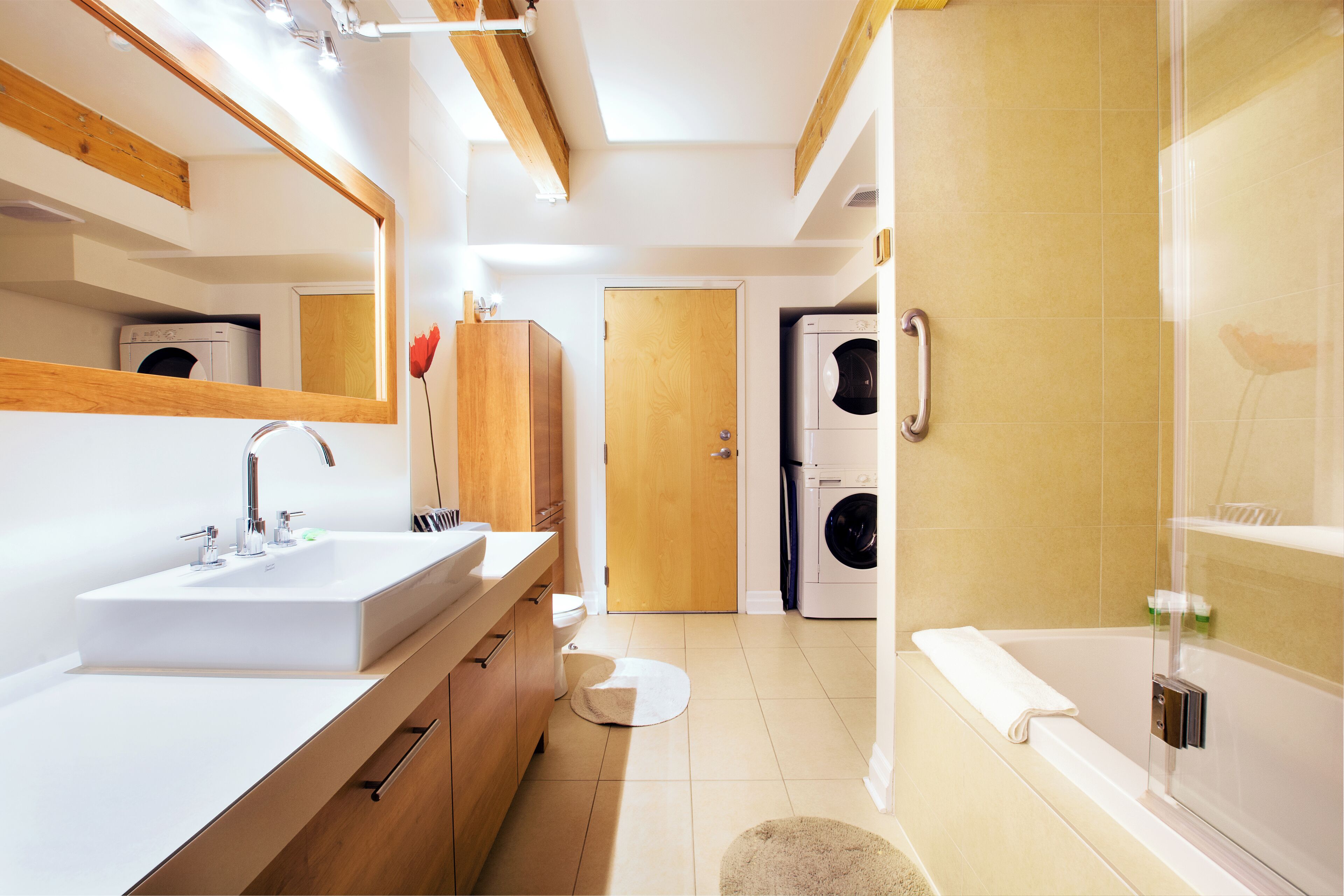 Une salle de bain moderne avec un grand lavabo, un miroir, des meubles en bois, des toilettes, un lave-linge et une baignoire.